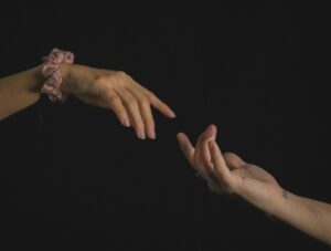 Minimalist photo of two hands reaching towards each other against a dark background.